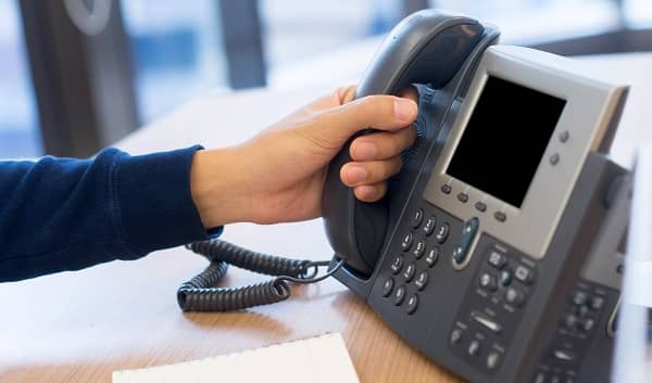 closeup of a hand on the receiver of an office phone