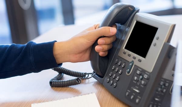 closeup of a hand on the receiver of an office phone