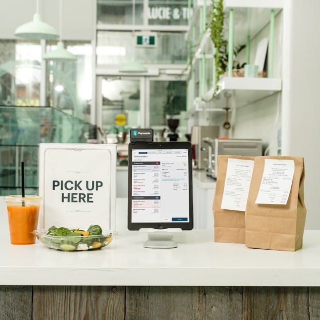 TouchBistro POS terminal displaying online orders next to prepared pickup orders at a restaurant counter.
