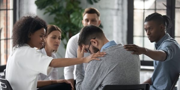 sad businessman being comforted by his coworkers