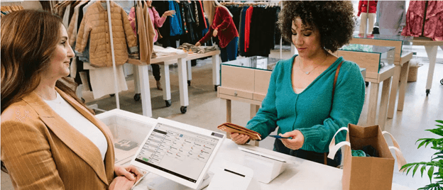 Retail employee using a Clover POS system to process a customer payment at a clothing store checkout counter.