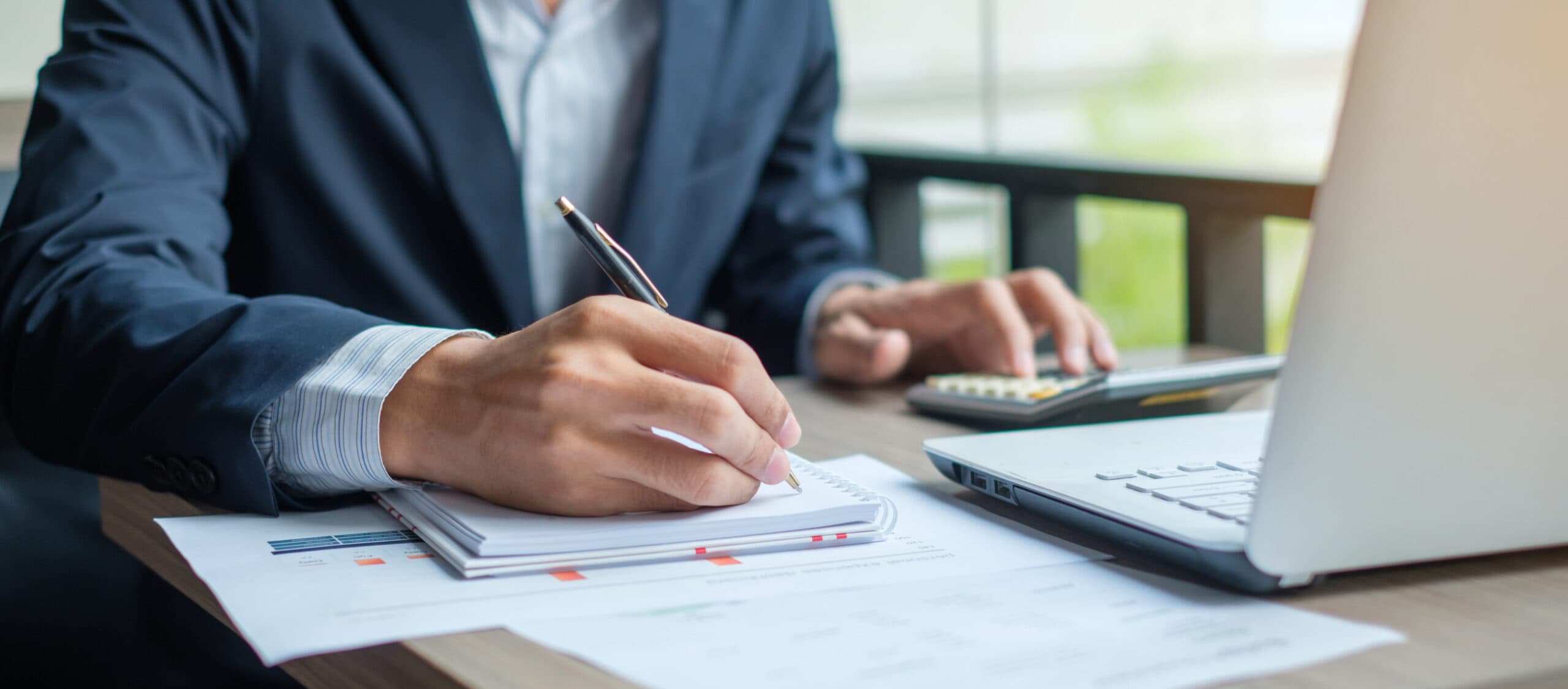 businessman writing in a notebook and typing on a calculator