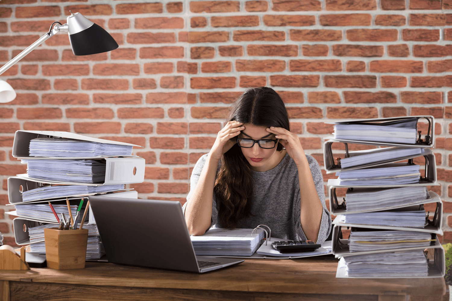 stressed businesswoman at a desk piled with binders