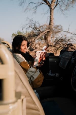Woman leaning up against a vehicle reading a travel guide